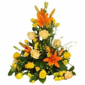 Färgsprakande hög begravningsdekoration med blommor i gult, orange och aprikosa färger. Arrangemanget finns hos Florister i Sverige bland begravningsblommorna.